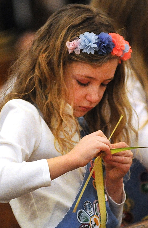 9-year-old Elizabeth Thompson, of Our Lady of Victory Parish, makes a cross from a blessed palm during Palm Sunday Mass at St Joseph Cathedral. (Dan Cappellazzo/Staff Photographer)